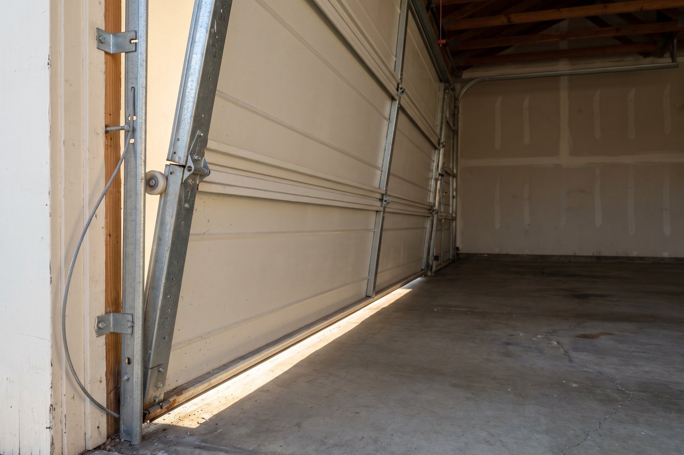 A garage door jammed part way up with the section stack skewed and one roller out of its channel.